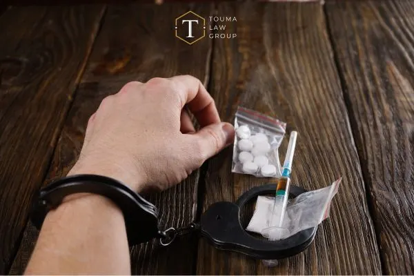 left hand in handcuff with a baggie of pills, bag of powder, and a needle laying to the right side on the table